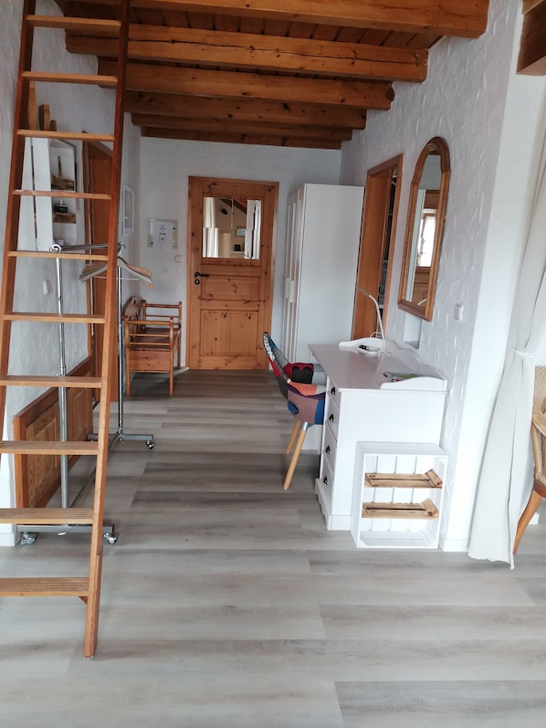 A room with a wooden ladder, a desk, a chair, and a door.
