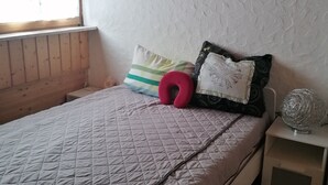 Un dormitorio con cama, almohadas, una mesita de noche y una ventana.