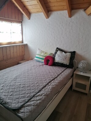 A bedroom with a bed, pillows, a nightstand, and a window.