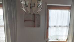 Un comedor con mesa de madera, cuatro sillas, una araña y una ventana con cortinas.