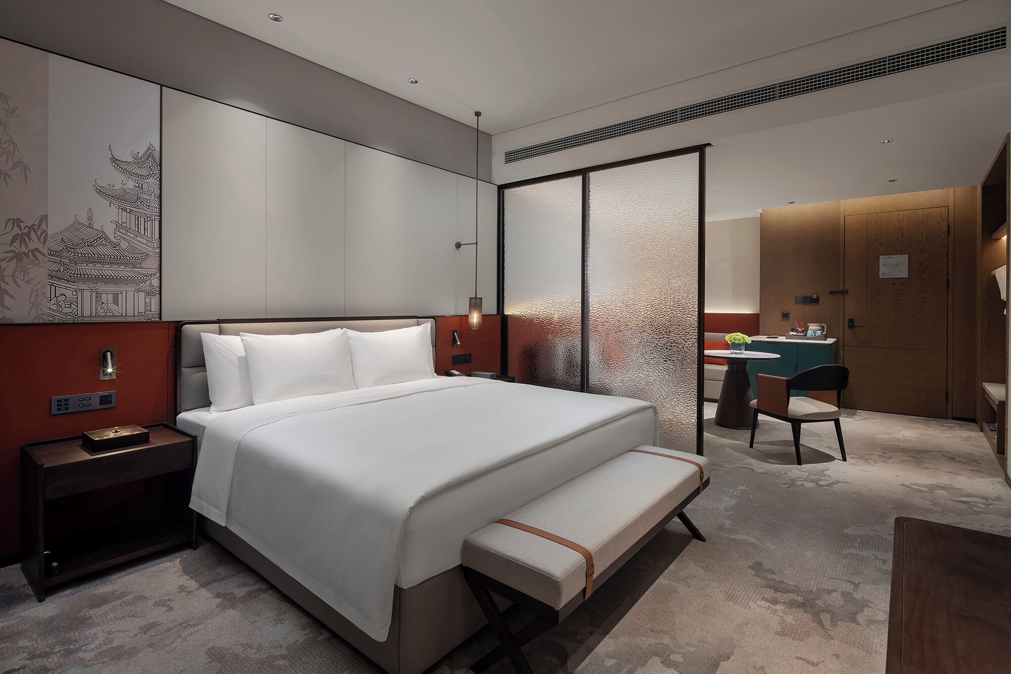 A modern hotel room with a large bed, bedside table, and a desk area with a chair.