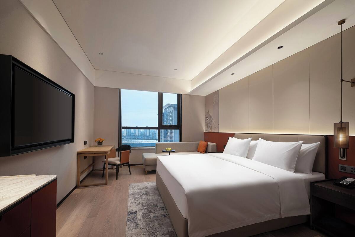 A modern hotel room with a large bed, a desk, a chair, and a TV.