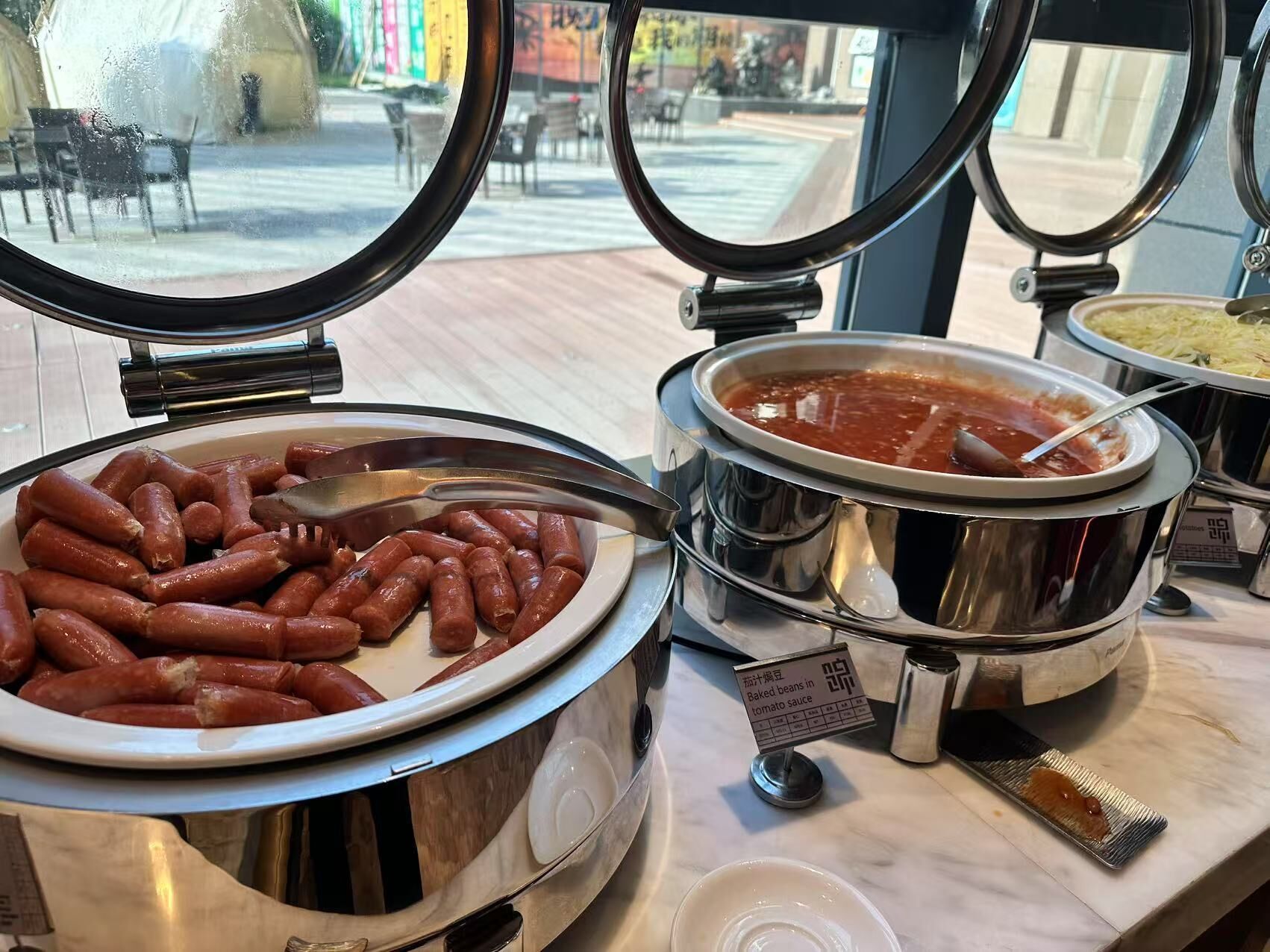 Un bufé con una variedad de alimentos, incluyendo salchichas y frijoles horneados en salsa de tomate.