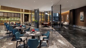 Un moderno vestíbulo de hotel con varias zonas de estar, incluyendo un bar y un espacio para comer.