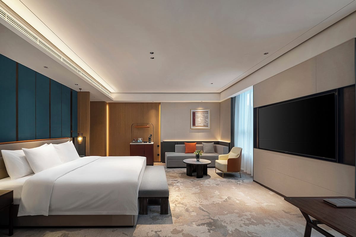 A modern hotel room with a large bed, a sofa, a TV, and a desk.