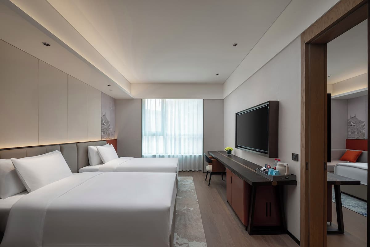 A modern hotel room with two beds, a desk, a TV, and a sofa.