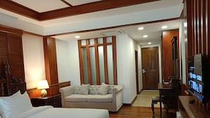 A hotel room with a large bed, a sofa, a desk, a television, and wooden paneling. - Phubarn VimarnVangvieng Resort (Vang Vieng)