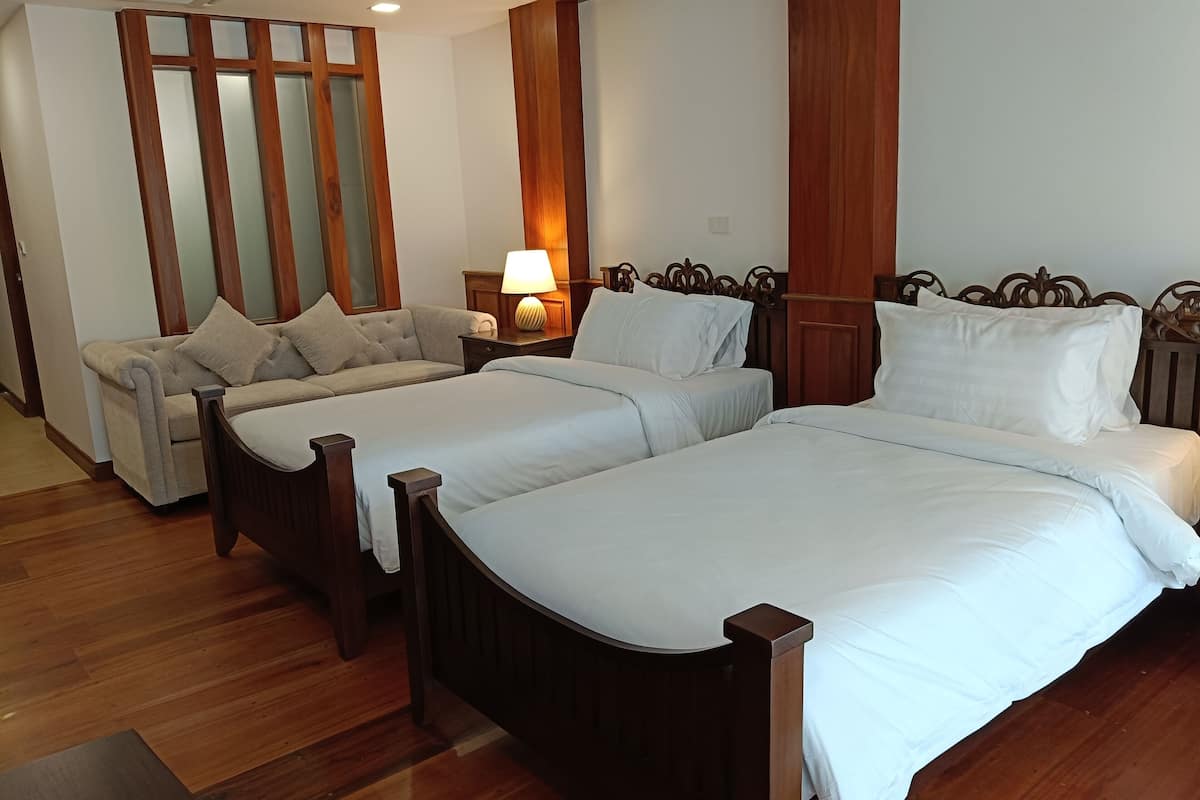 Ein Hotelzimmer mit zwei Einzelbetten, einem Schlafsofa und einem Nachttisch mit Lampe.