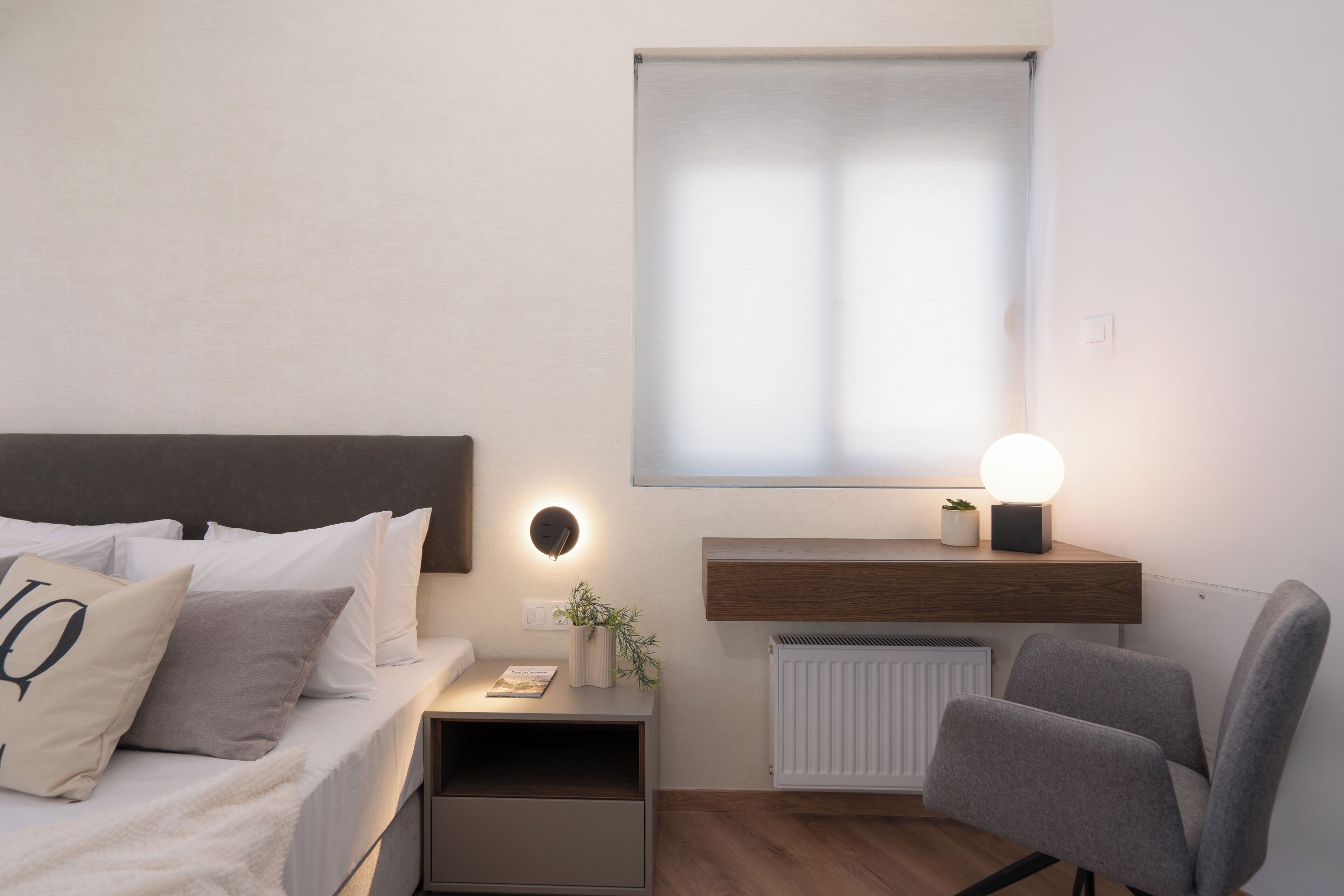 A modern bedroom with a bed, bedside table, lamp, and a window with blinds.