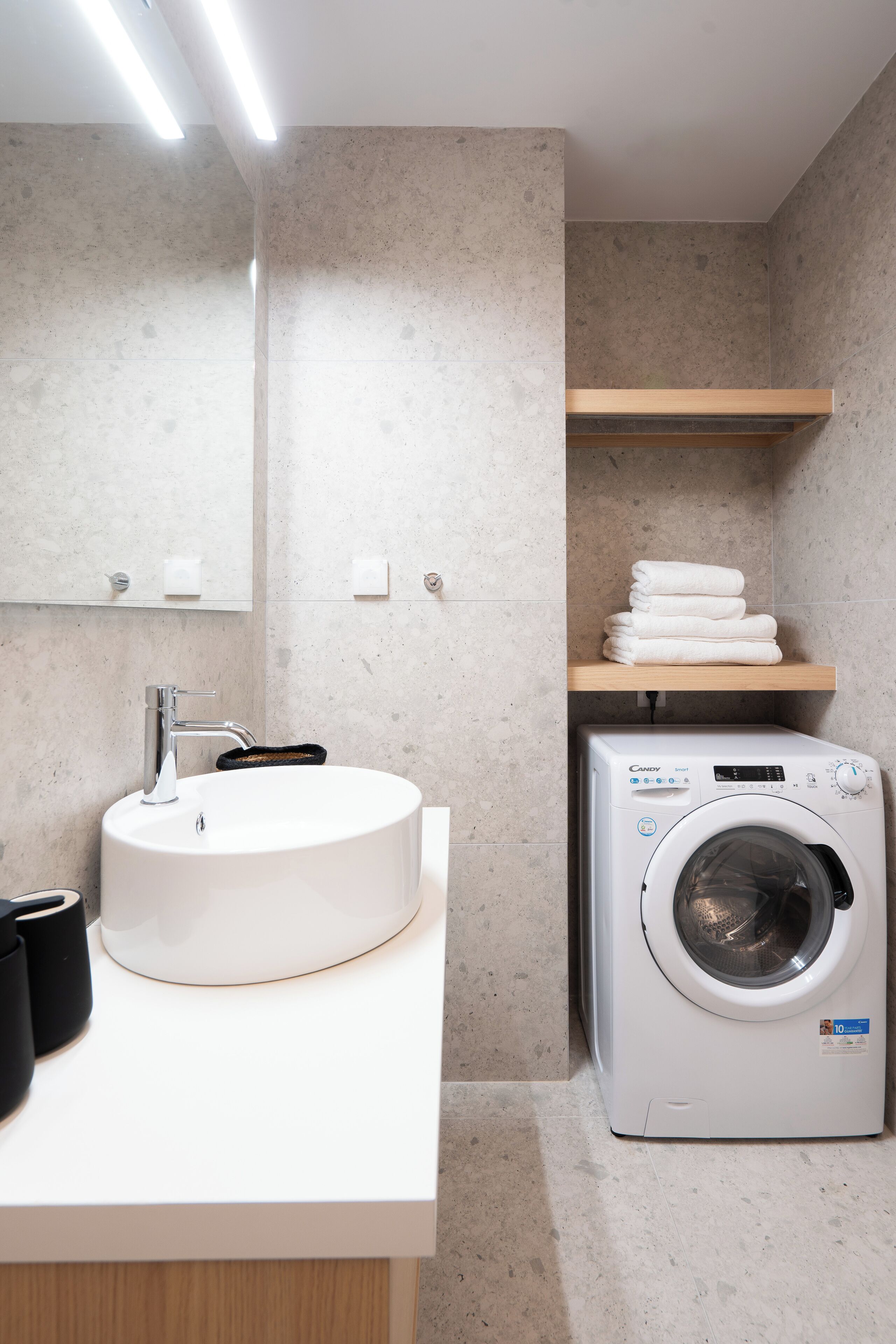 A modern bathroom with a round sink, a built-in washing machine, and a mirror above the sink.