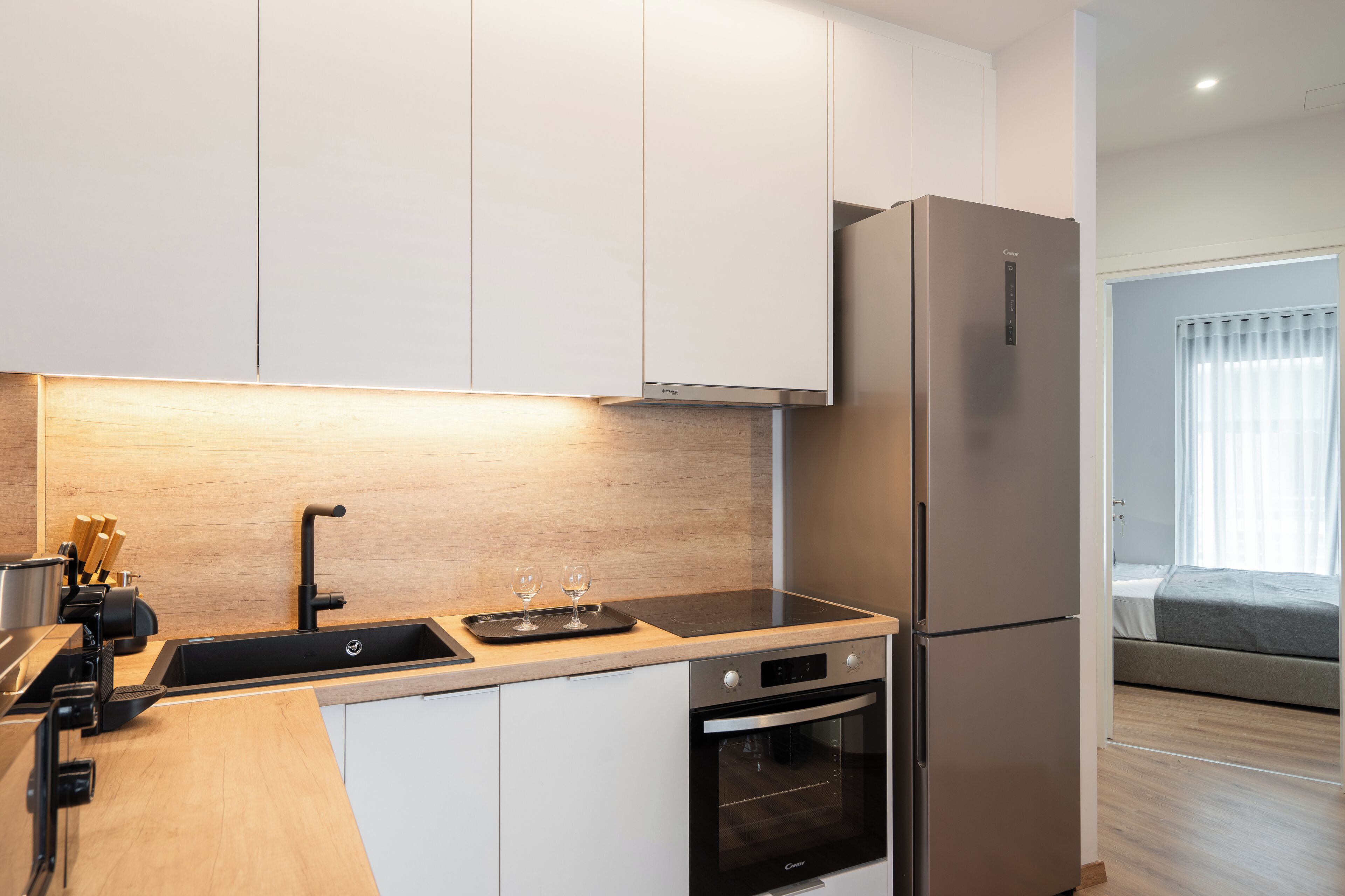 A modern kitchen with white cabinets, a stainless steel refrigerator, and a built-in oven.