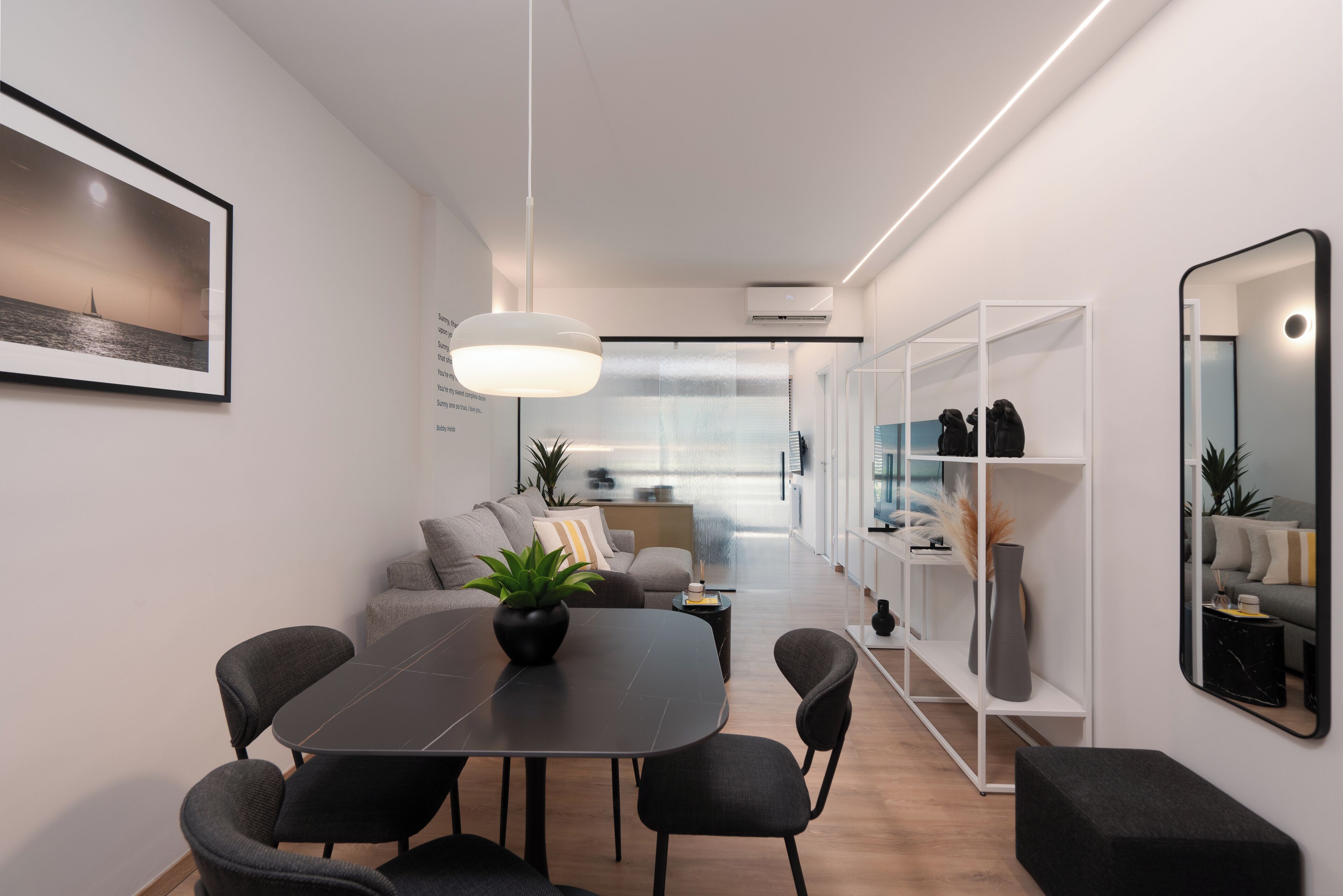 A modern, well-lit interior with a dining area, a sofa, and a bookshelf.