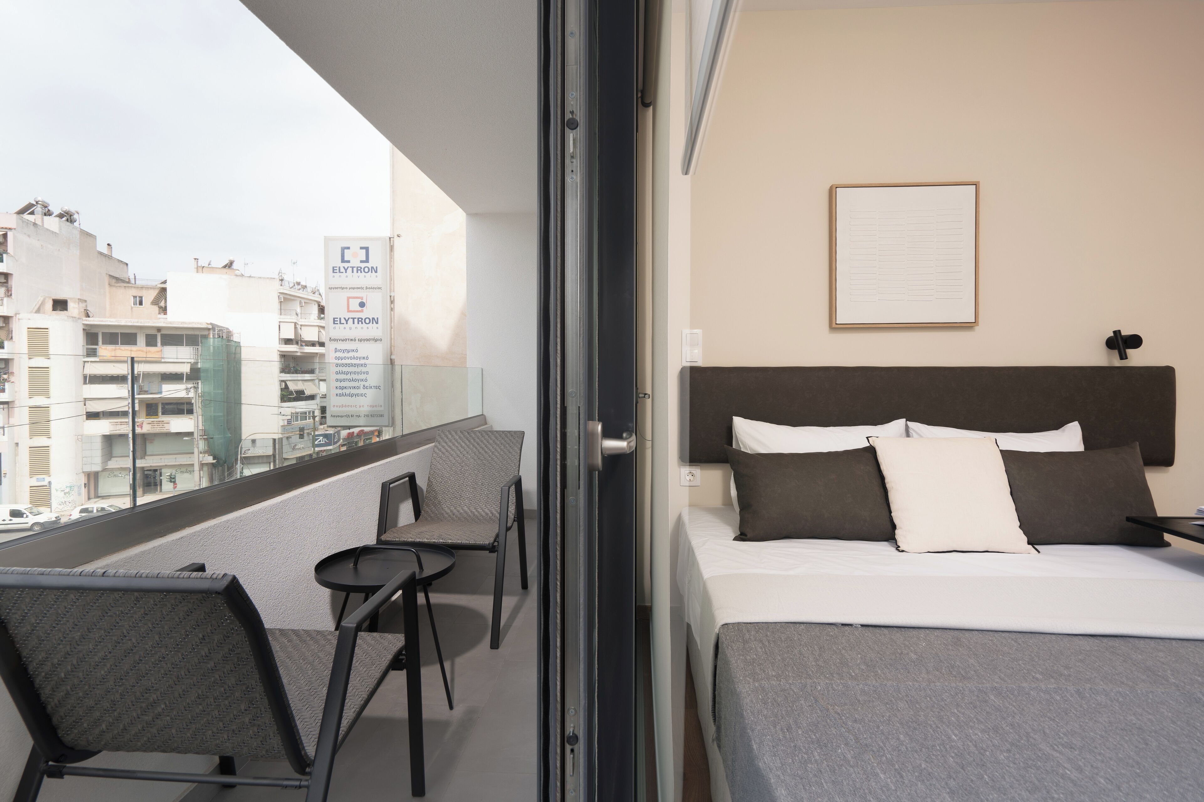 Una habitació d'hotel amb un balcó, un llit amb almoades, una cadira i un quadre al mur.