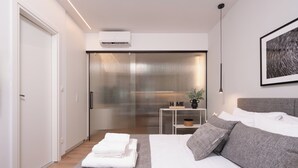 Un dormitorio moderno con una cama, una mesita de noche con una planta y un aire acondicionado de pared.