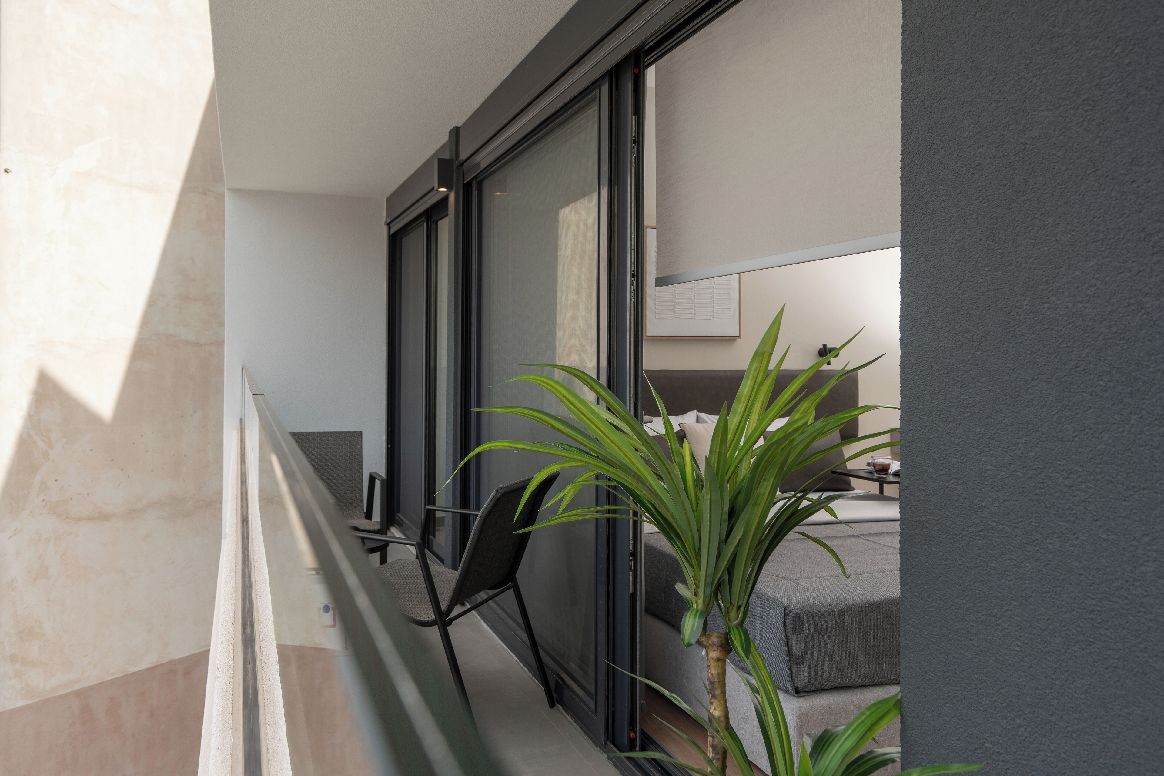 Un balcon avec un fauteuil moderne, une plante en pot et un aperçu d’un espace de vie comprenant un canapé et une table.