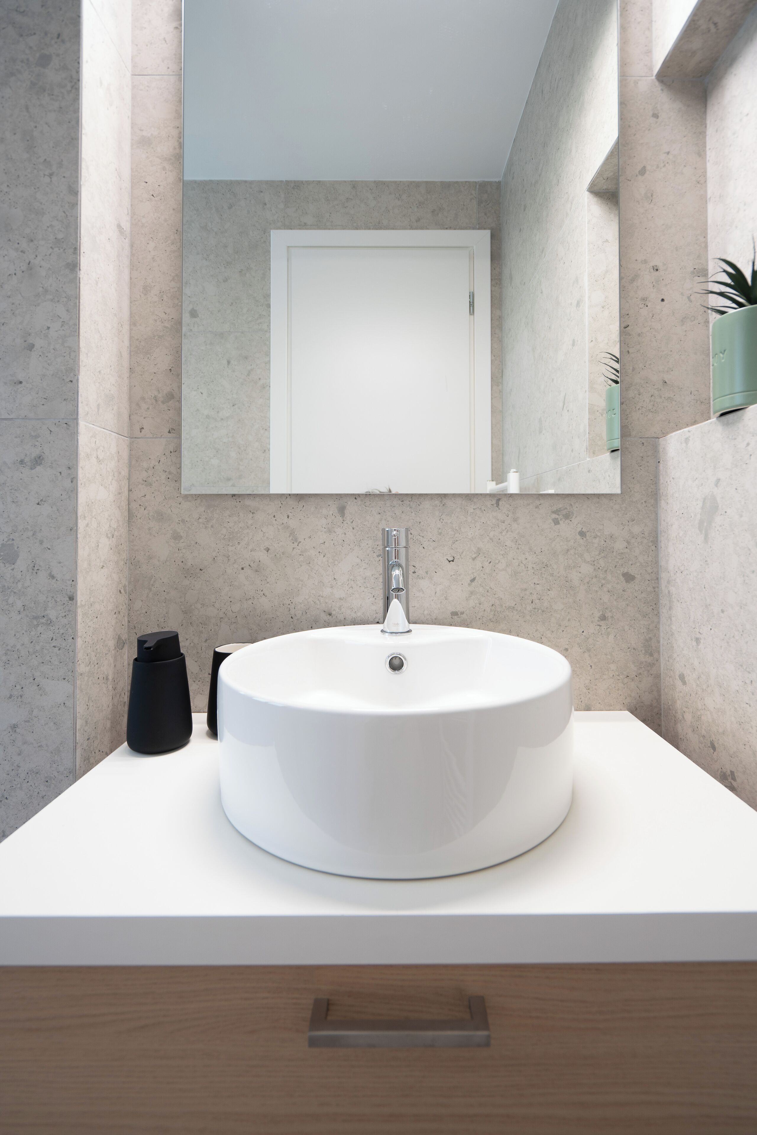 Une salle de bain moderne avec un lavabo rond blanc, un miroir au-dessus et un meuble en bois en dessous.