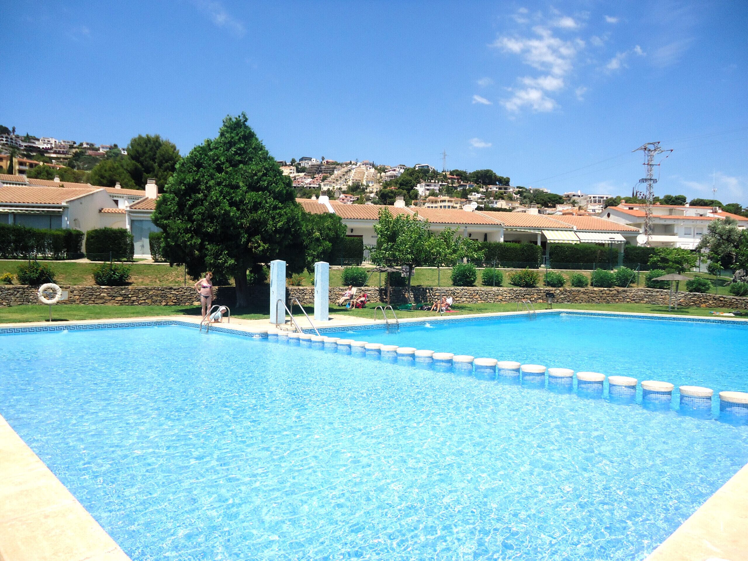 A swimming pool with a clear blue water, surrounded by a stone wall and a grassy area.