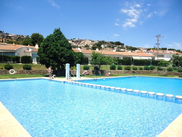 A swimming pool with a clear blue water, surrounded by a stone wall and a grassy area.
