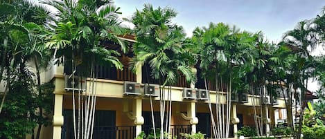 A multi-story hotel with air conditioning units on the exterior, surrounded by lush greenery.