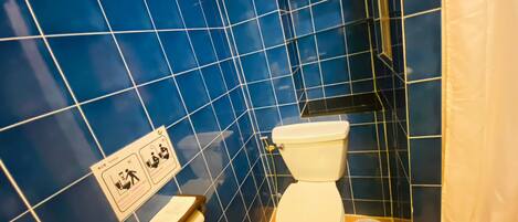 A bathroom with blue tiled walls, a white toilet, a hand dryer, and a trash bin.