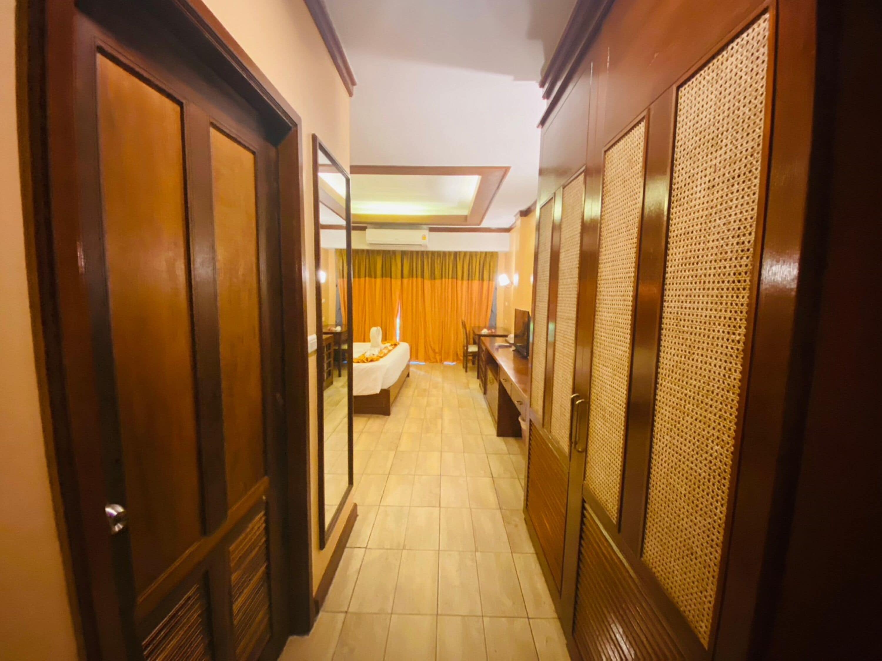 Corridoio di un hotel con porte in legno, un letto sullo sfondo e una scrivania con un computer.