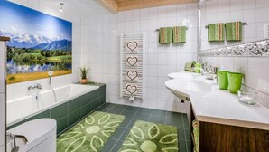 A modern bathroom with a large bathtub, a toilet, a sink, and a shower. There is a green patterned rug on the floor, and towels hanging on a rack. - Vacation apartment Bergparadies 154 sqm for max. 4 persons (Obing)