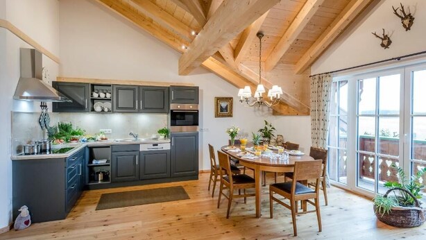 A kitchen with dark cabinets, a wooden ceiling, and a dining area with a table and chairs. - Vacation apartment Bergparadies 154 sqm for max. 4 persons (Obing)