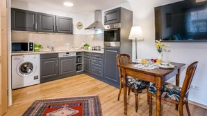 Una cocina compacta con armarios grises, horno integrado, lavadora y comedor con mesa y sillas.