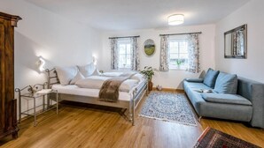 Un dormitorio con cama, mesita de noche, sofá, espejo y ventana con cortinas.