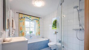 Un baño moderno con bañera, inodoro y zona de ducha con mampara de vidrio.