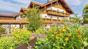 Un chalet traditionnel avec une façade en bois, un balcon agrémenté de jardinières et un jardin où poussent différentes variétés de fleurs.