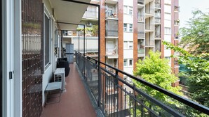 Ein Balkon mit Blick auf ein mehrstöckiges Wohngebäude, Gartenmöbel und einem Metallgeländer.