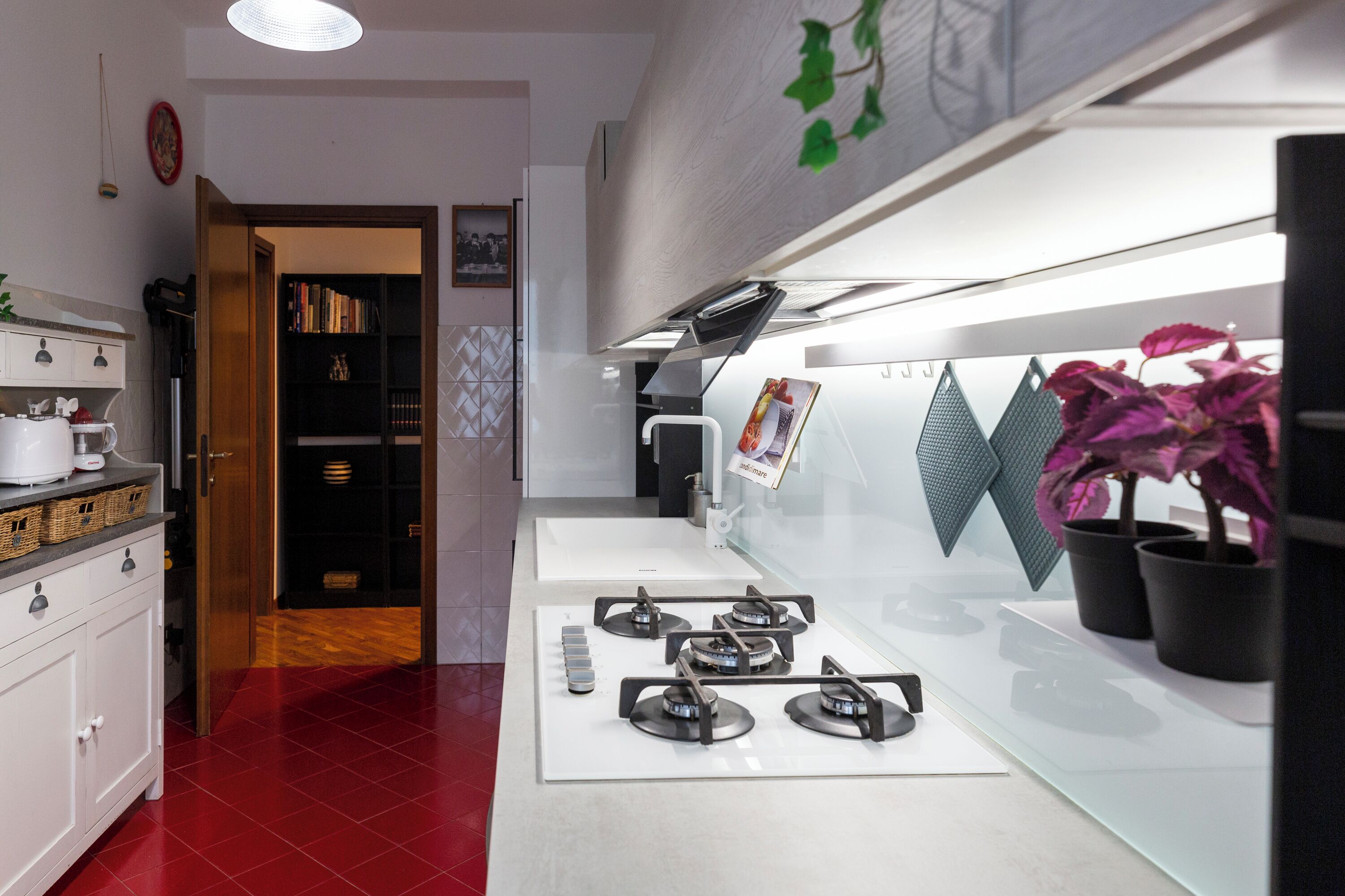 A modern kitchen with a gas stove, white cabinets, and a red-tiled floor.
