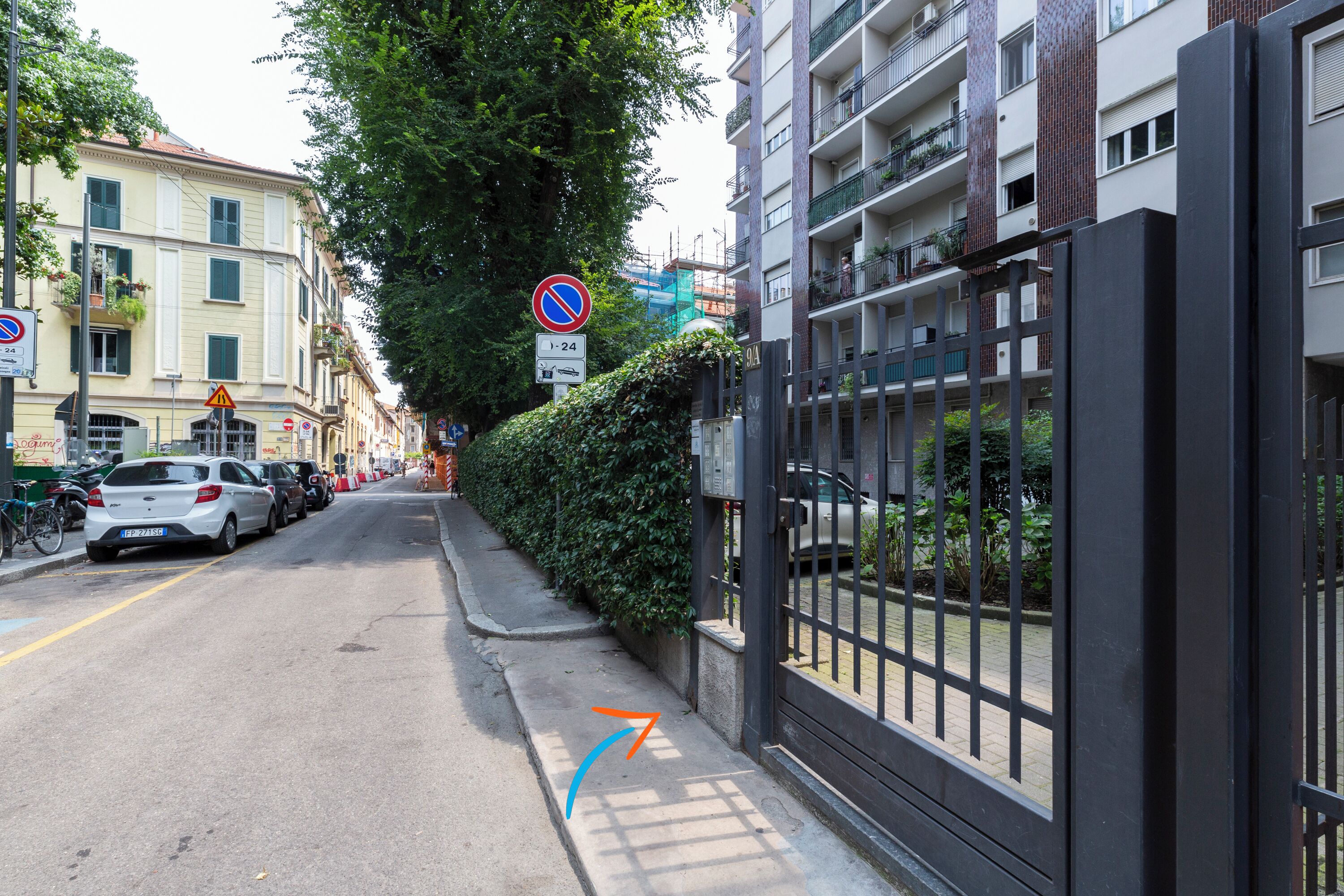 A street view with parked cars, a no parking sign, and a gated entrance to a building.