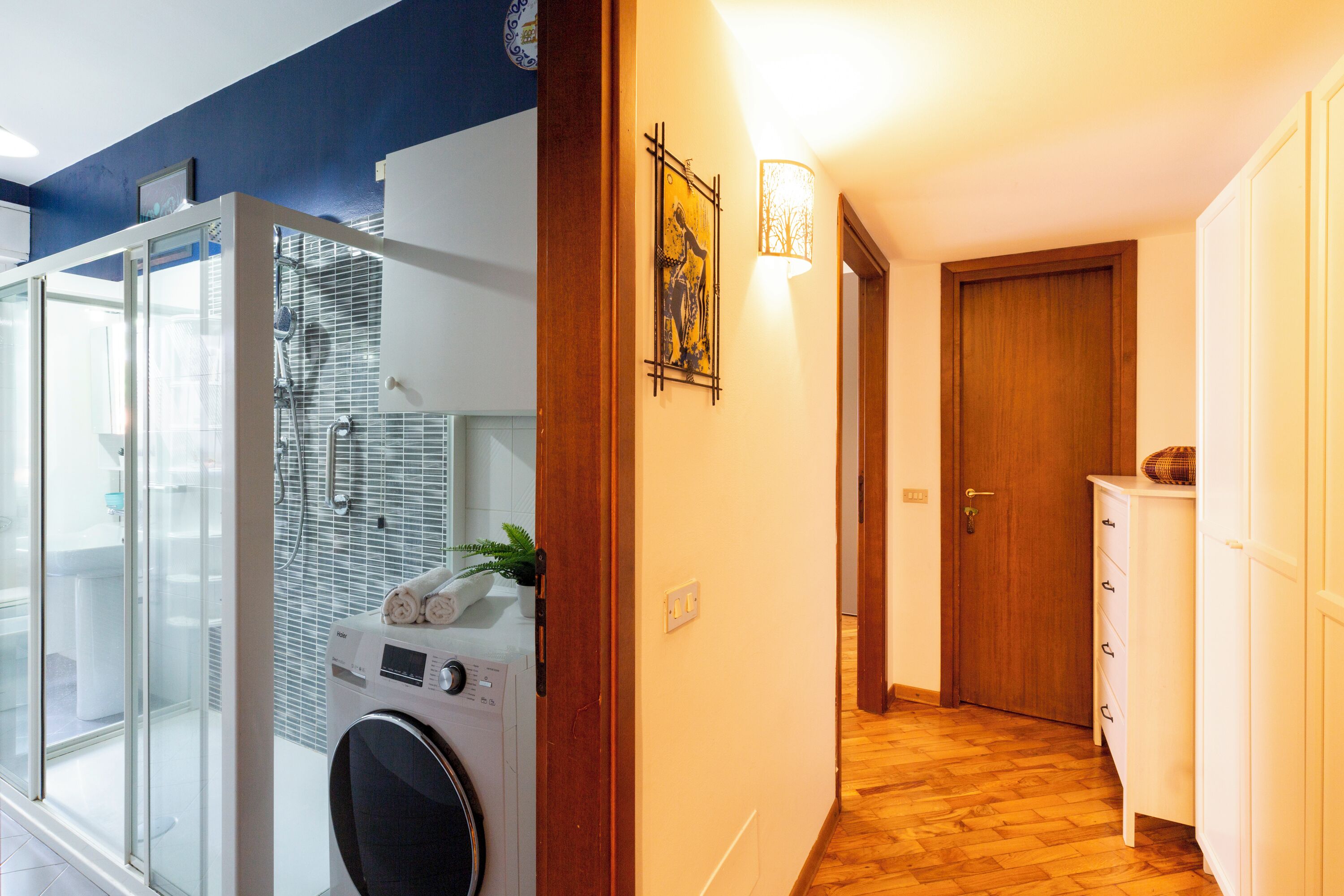 A laundry area with a washing machine and dryer, a glass shower enclosure, and a wooden floor.