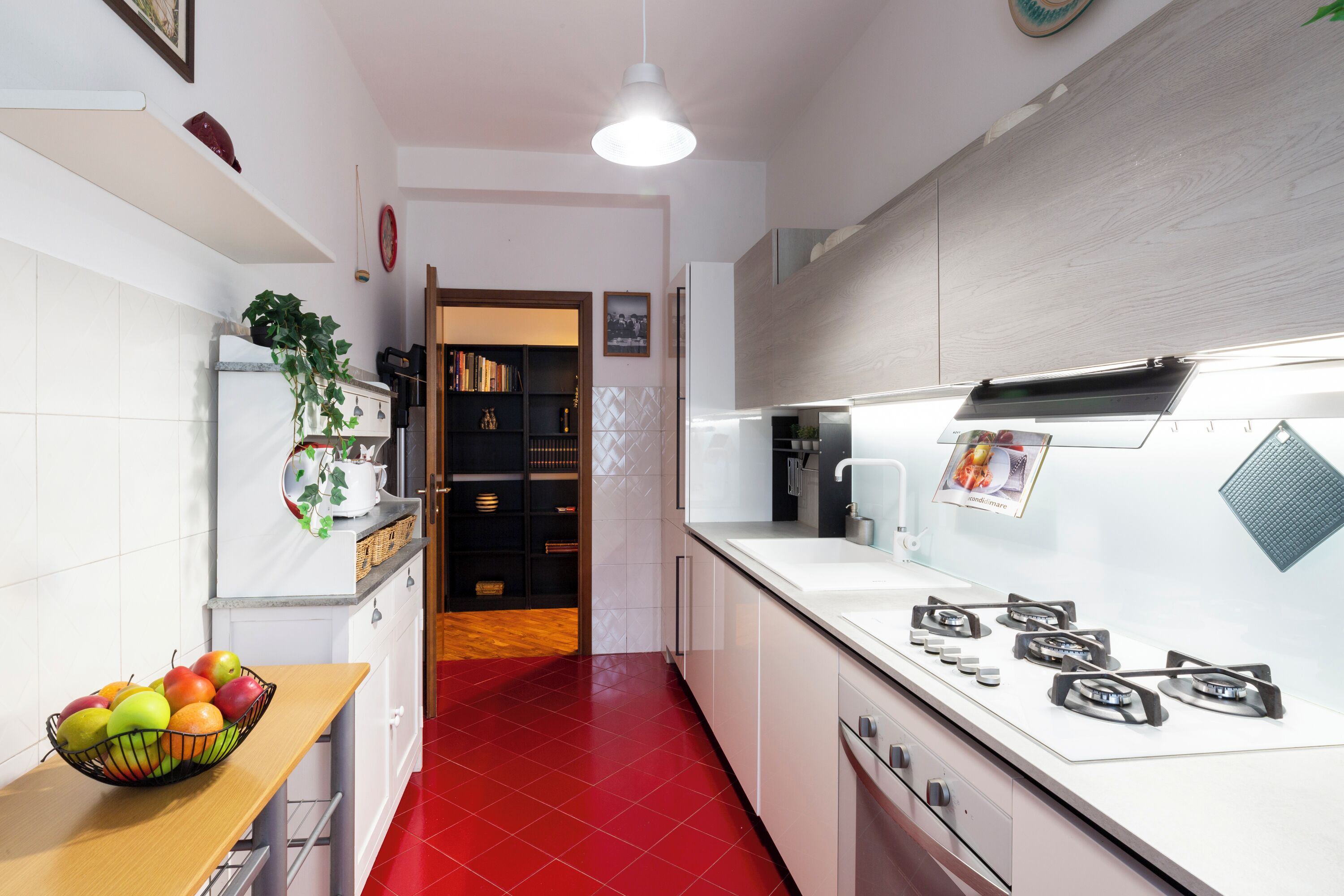 A modern kitchen with white cabinets, a red tiled floor, a wooden countertop, and a gas stove.