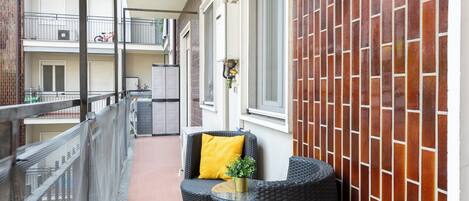 A balcony with wicker furniture and a yellow cushion, a tiled wall, and a metal railing.