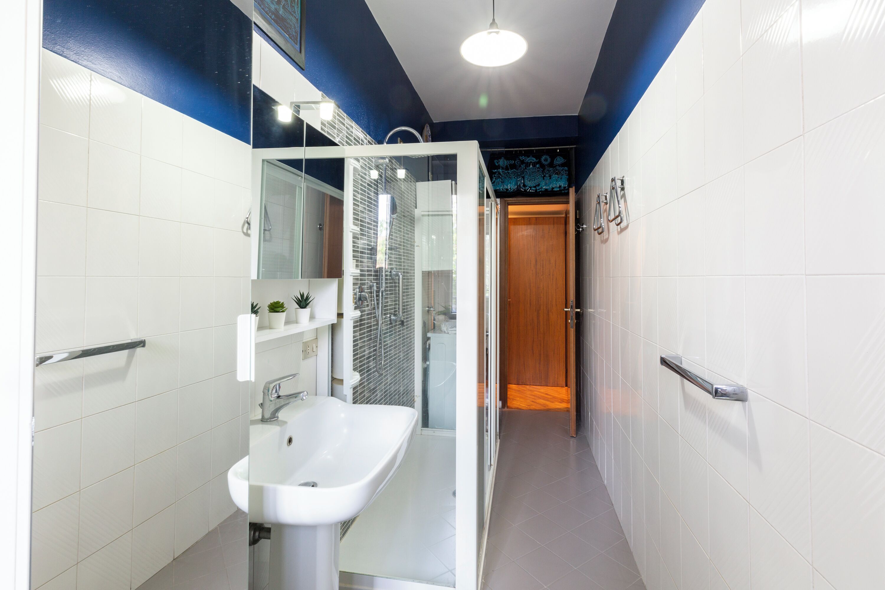 Casa de banho moderna com lavatório branco, cabine de duche em vidro e porta de madeira que dá para outro espaço.