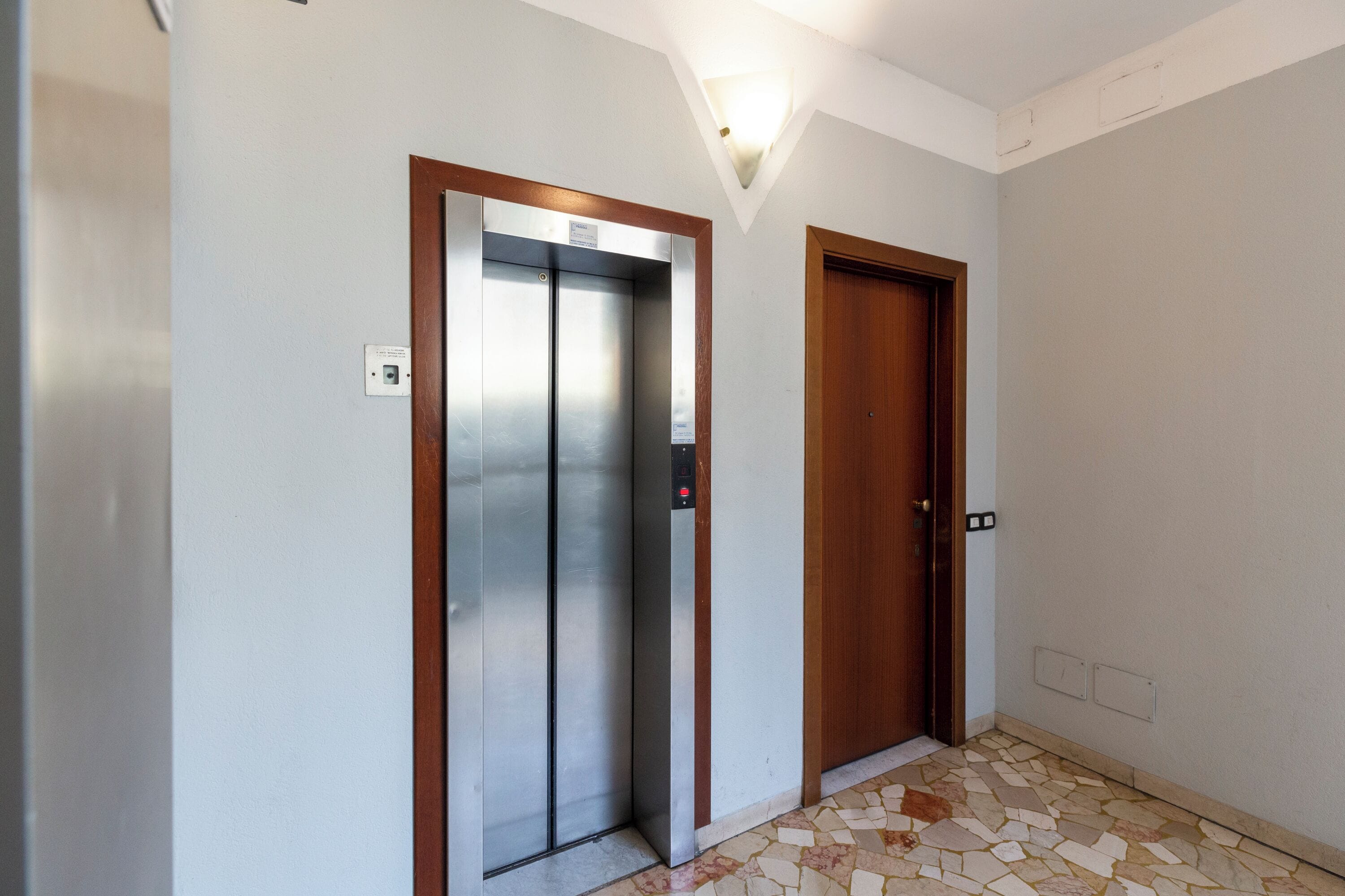 Un ascenseur et une porte dans un couloir dont le sol est recouvert de carreaux.