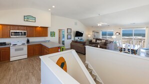 Una cocina moderna con armarios de madera, microondas y estufa. Hay un comedor con mesa y sillas, y una sala de estar con sofá y televisor.