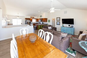 A spacious living area with a dining table, sofas, a TV, and a kitchen in the background. - An Octopus Hug, Oceanfront, Dog Friendly, 4 Bd. (Virginia Beach)