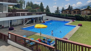 Un hotel moderno con piscina, zona de estar exterior y vistas a las montañas.