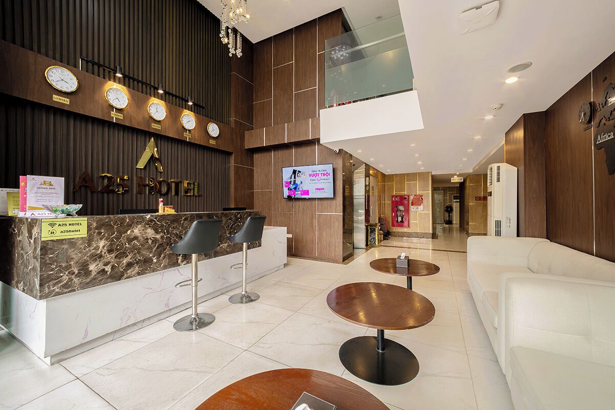 Een hotel receptie met een marmeren balie, zwarte stoelen, een televisiescherm en een modern interieur.