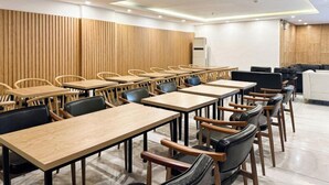 Ein moderner Konferenzraum mit Holzpaneelen, mehreren Tischen und Stühlen sowie deckenintegrierter Beleuchtung.