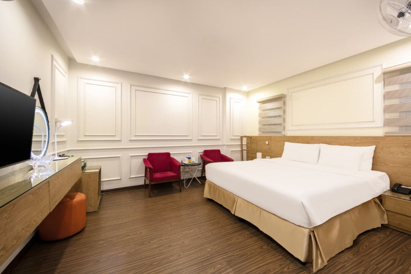 Une chambre d’hôtel avec un grand lit, un bureau avec un miroir, deux chaises rouges et une petite table.