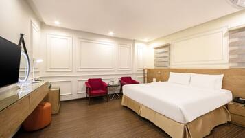 Une chambre d’hôtel avec un grand lit, un bureau avec un miroir, deux chaises rouges et une petite table.