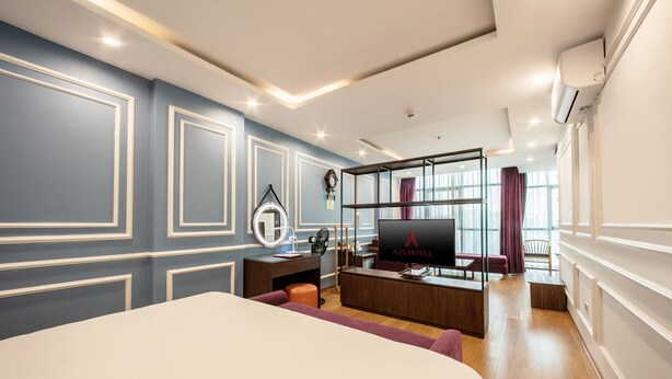 Ein modernes Hotelzimmer mit einem großen Bett, einem Schreibtisch mit Computer, einem Fernseher und einer Sitzecke mit Blick auf die Stadt.