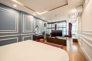Une chambre d’hôtel moderne dotée d’un grand lit, d’un bureau avec un ordinateur, d’une télévision et d’un coin salon offrant une vue sur la ville.