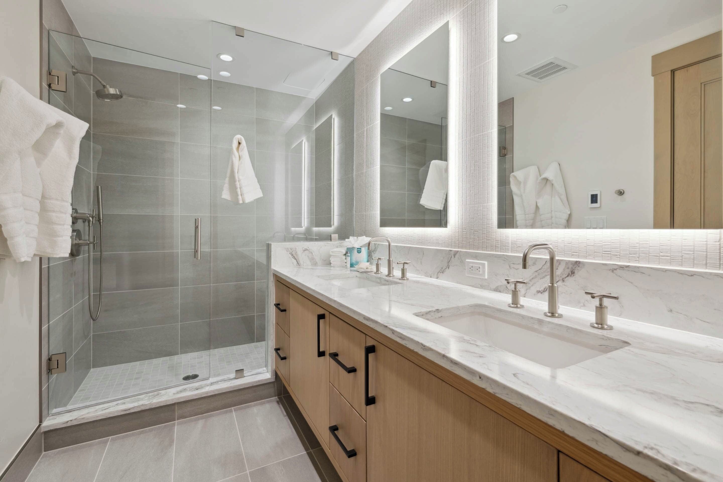 A modern bathroom with a glass-enclosed shower, a large mirror, and a marble countertop.