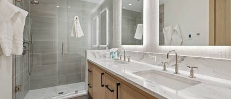 A modern bathroom with a glass-enclosed shower, a large mirror, and a marble countertop.